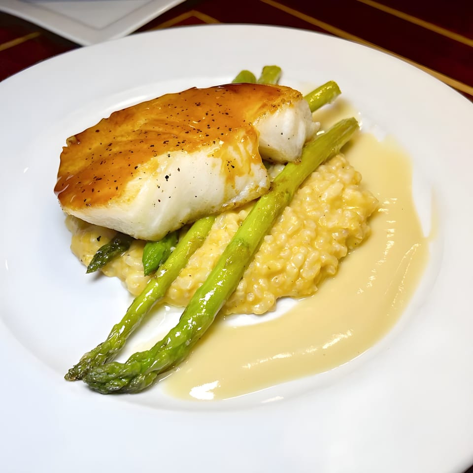 Pan-seared Mad Fish halibut with asparagus, creamy risotto, and a light sauce on a white plate.