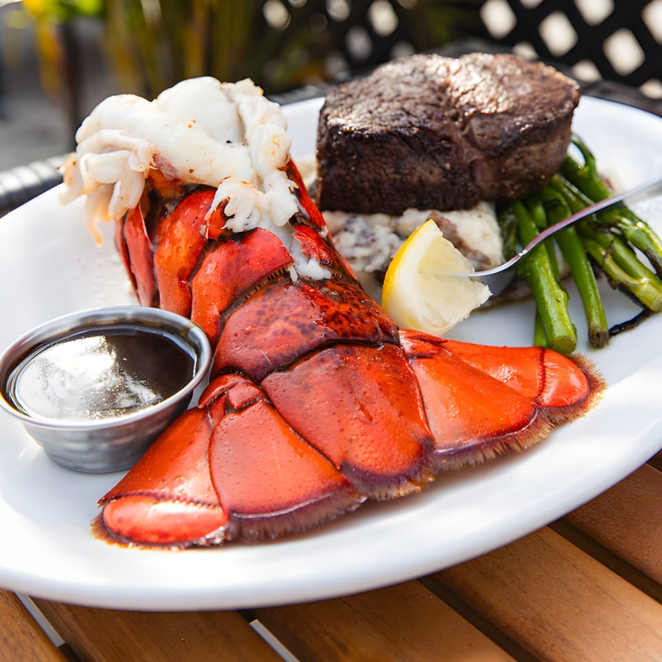 Mad Fish surf and turf with lobster tail, steak, asparagus, and lemon on a white plate.