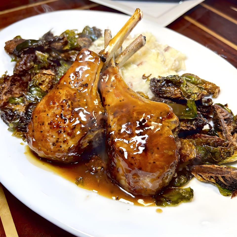 Two glazed lamb chops with mashed potatoes and roasted Brussels sprouts on a white plate.