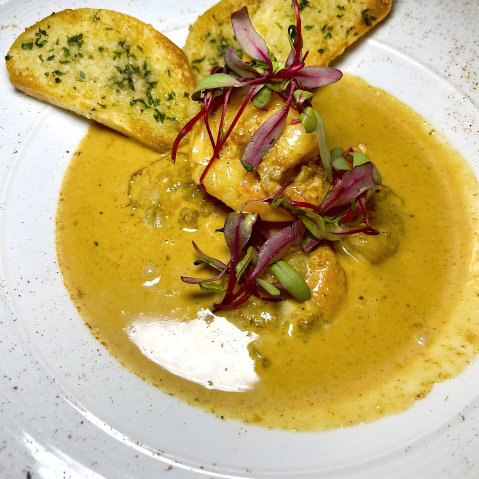 Mad Fish shrimp dish with yellow sauce, red and green garnish, and two pieces of garlic bread.
