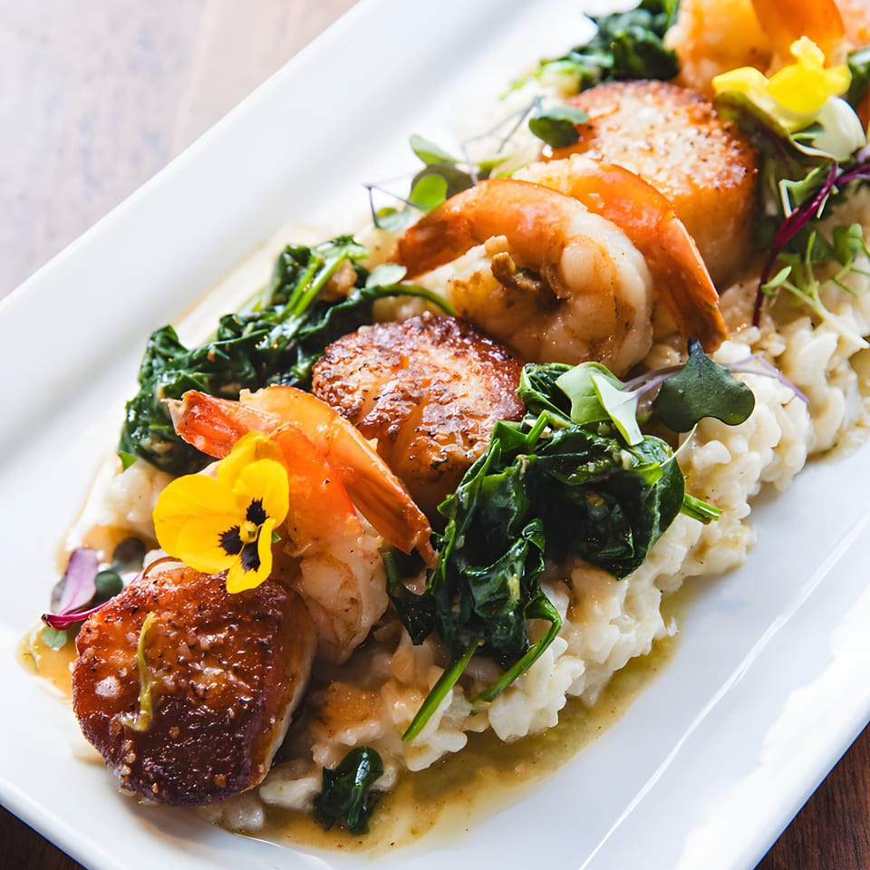 Seared scallops and shrimp over creamy risotto with spinach and a yellow edible flower.