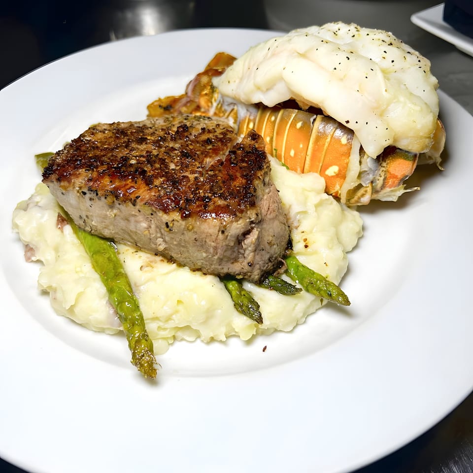 A Mad Fish surf and turf dish with steak, lobster tail, mashed potatoes, and asparagus.